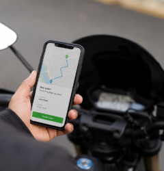 Delivery driver holding a smartphone with a navigation and order notification screen next to a scooter during a food delivery shift.