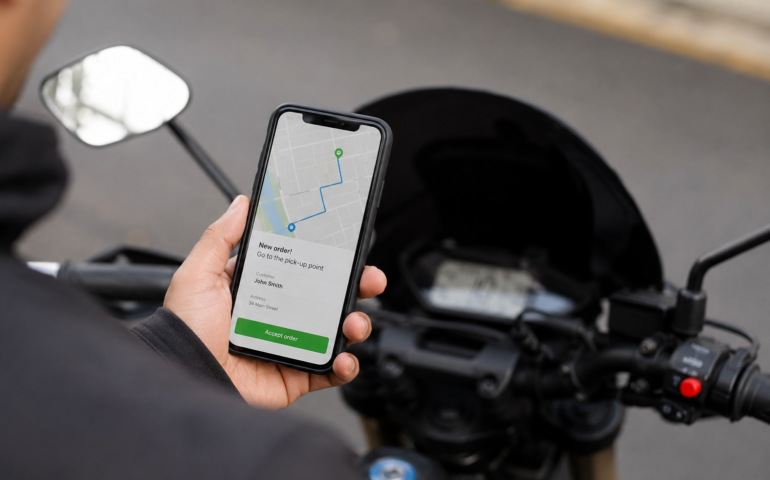 Delivery driver holding a smartphone with a navigation and order notification screen next to a scooter during a food delivery shift.